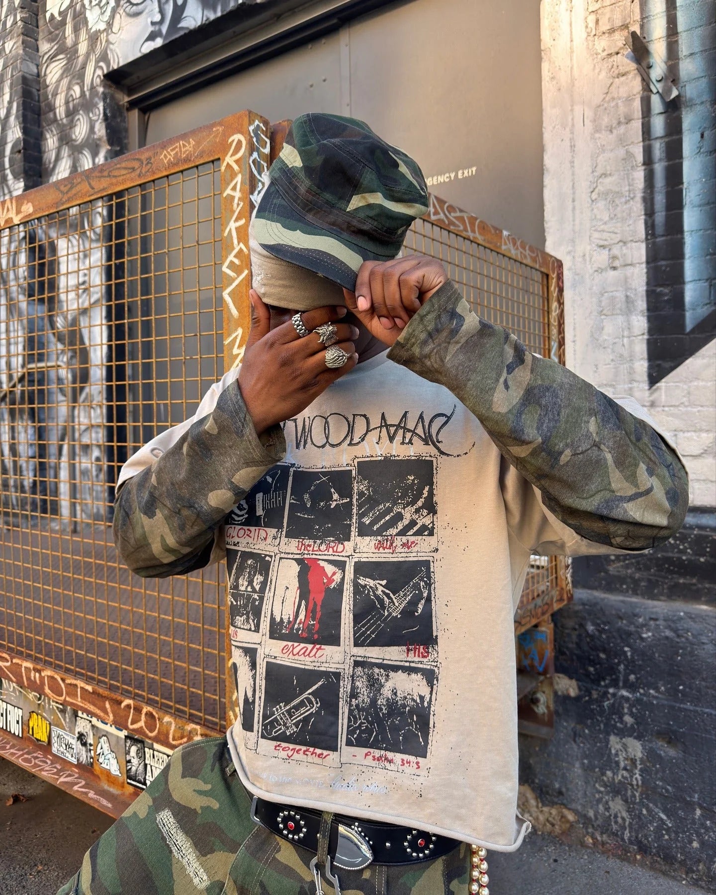 Person in urban setting wears a Distressed Grunge Layered T-Shirt, featuring a camo long sleeve under a graphic tee with vintage distressed design.