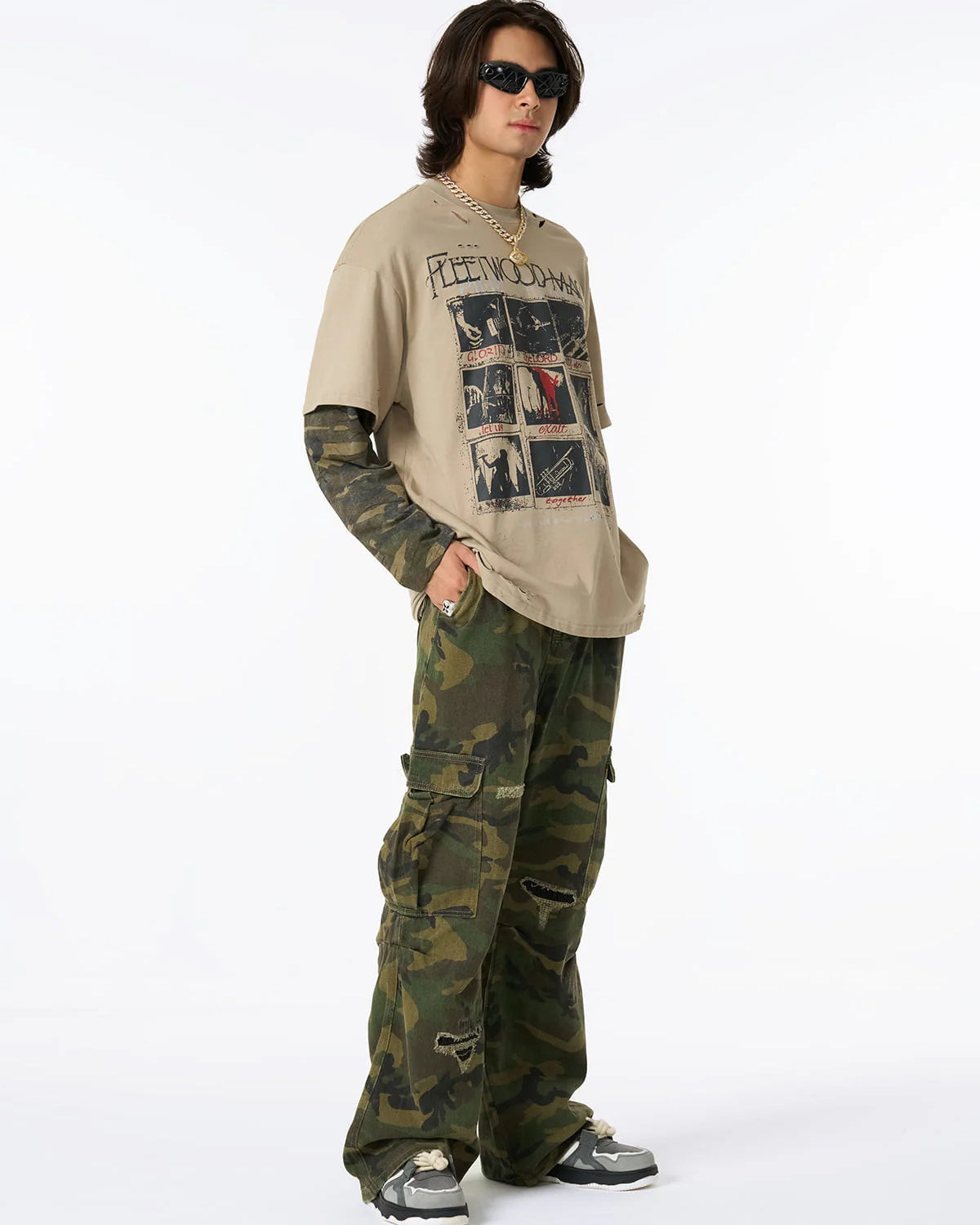 Model in Distressed Grunge Layered T-Shirt with graphic design, camo long sleeves, camouflage cargo pants, chunky sneakers, gold chain, sunglasses, and silver ring.