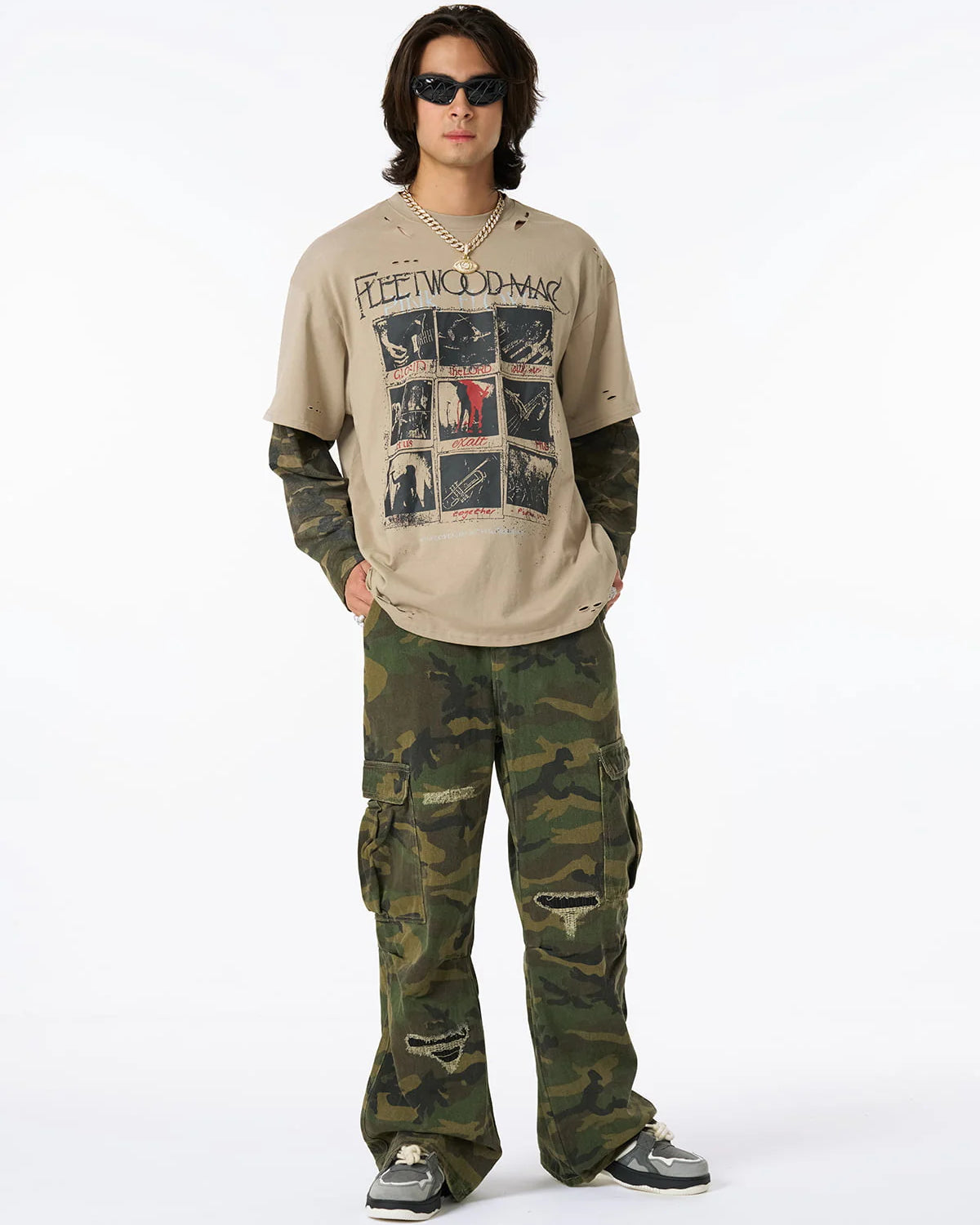 Young man models Distressed Grunge Layered T-Shirt with vintage Fleetwood Mac print, camo long sleeves, and intentional distressing, styled with camo pants and chunky sneakers.