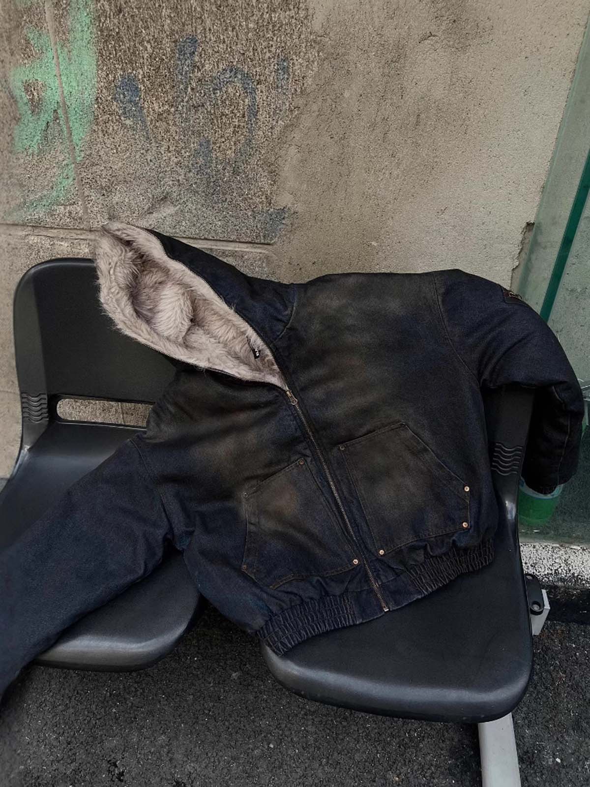 Distressed Washed Faux Fur Winter Jacket with a hood, fleece-lined interior, front pockets, and elasticized hem, displayed on plastic seats against a graffiti-marked wall.