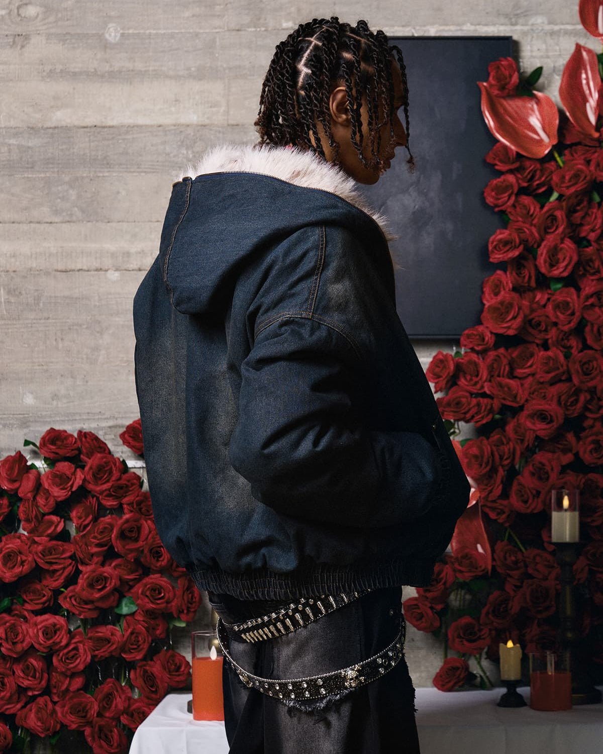 Person in profile wearing the Distressed Washed Faux Fur Winter Jacket with a fluffy collar, styled with black pants and surrounded by roses and candles.