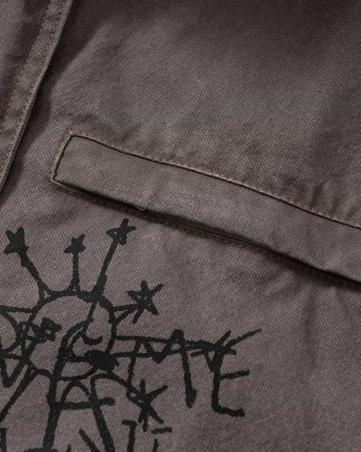 Graphic Graffiti High Neck Street Jacket highlighting a grey canvas-style fabric with a horizontal pocket flap and a black, hand-drawn sunburst graphic below it.