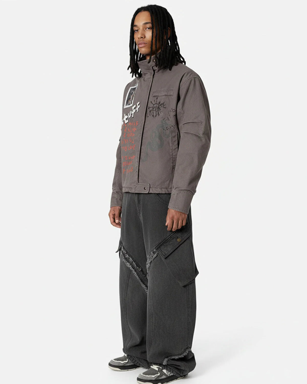 Young man models the Graphic Graffiti High Neck Street Jacket, featuring bold doodles and a high collar, paired with oversized cargo jeans and dark sneakers.