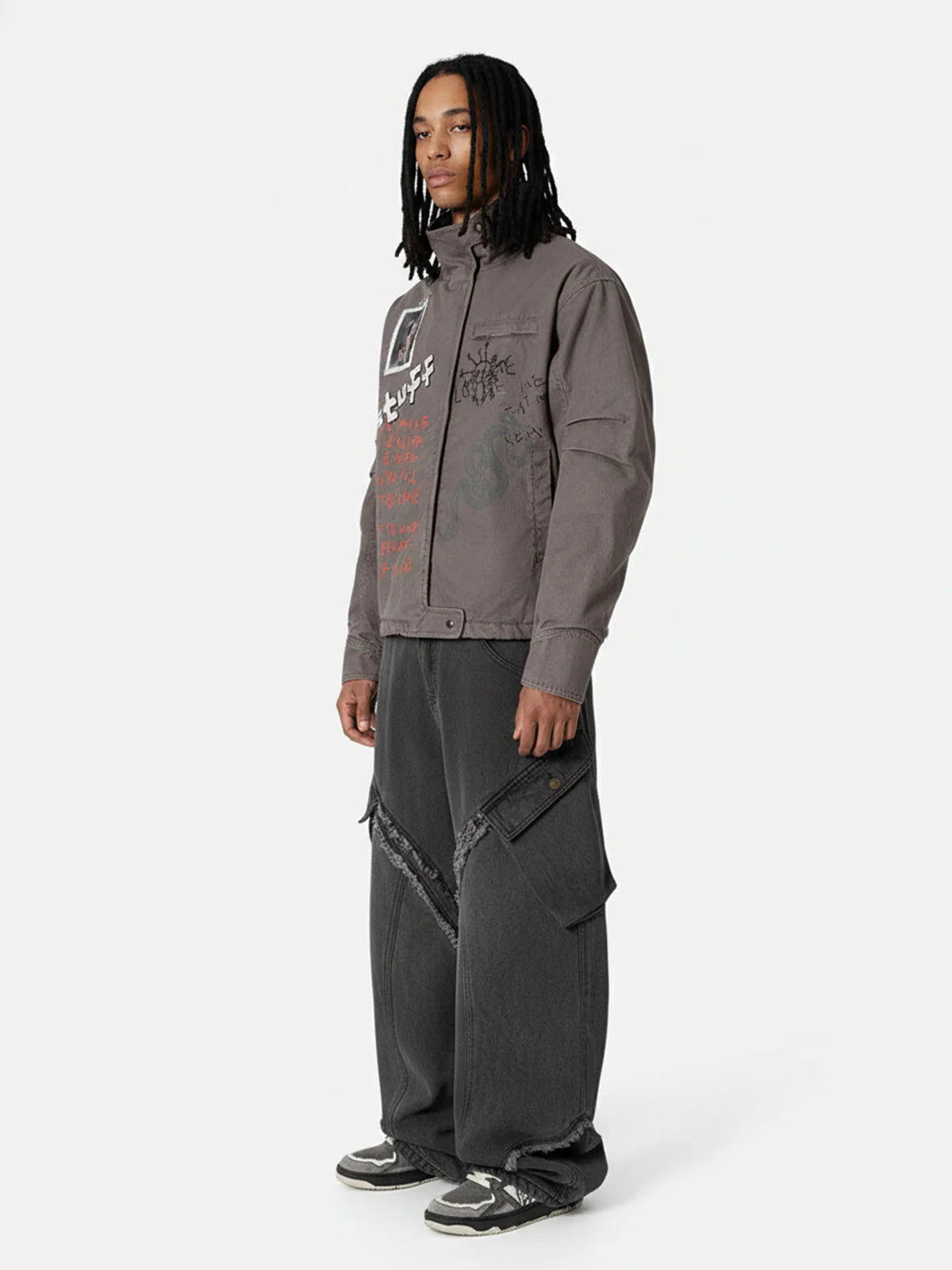 Young man models the Graphic Graffiti High Neck Street Jacket, featuring bold doodles and a high collar, paired with oversized cargo jeans and dark sneakers.
