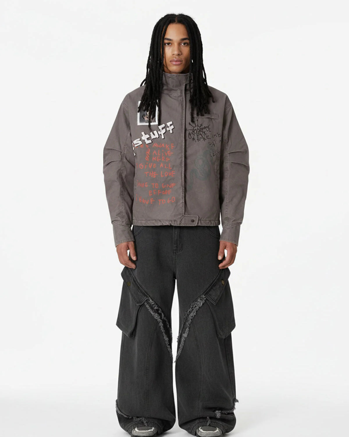 Young man wearing a Graphic Graffiti High Neck Street Jacket with hand-drawn graphics, wide-leg black cargo jeans, and chunky sneakers, showcasing bold streetwear style.