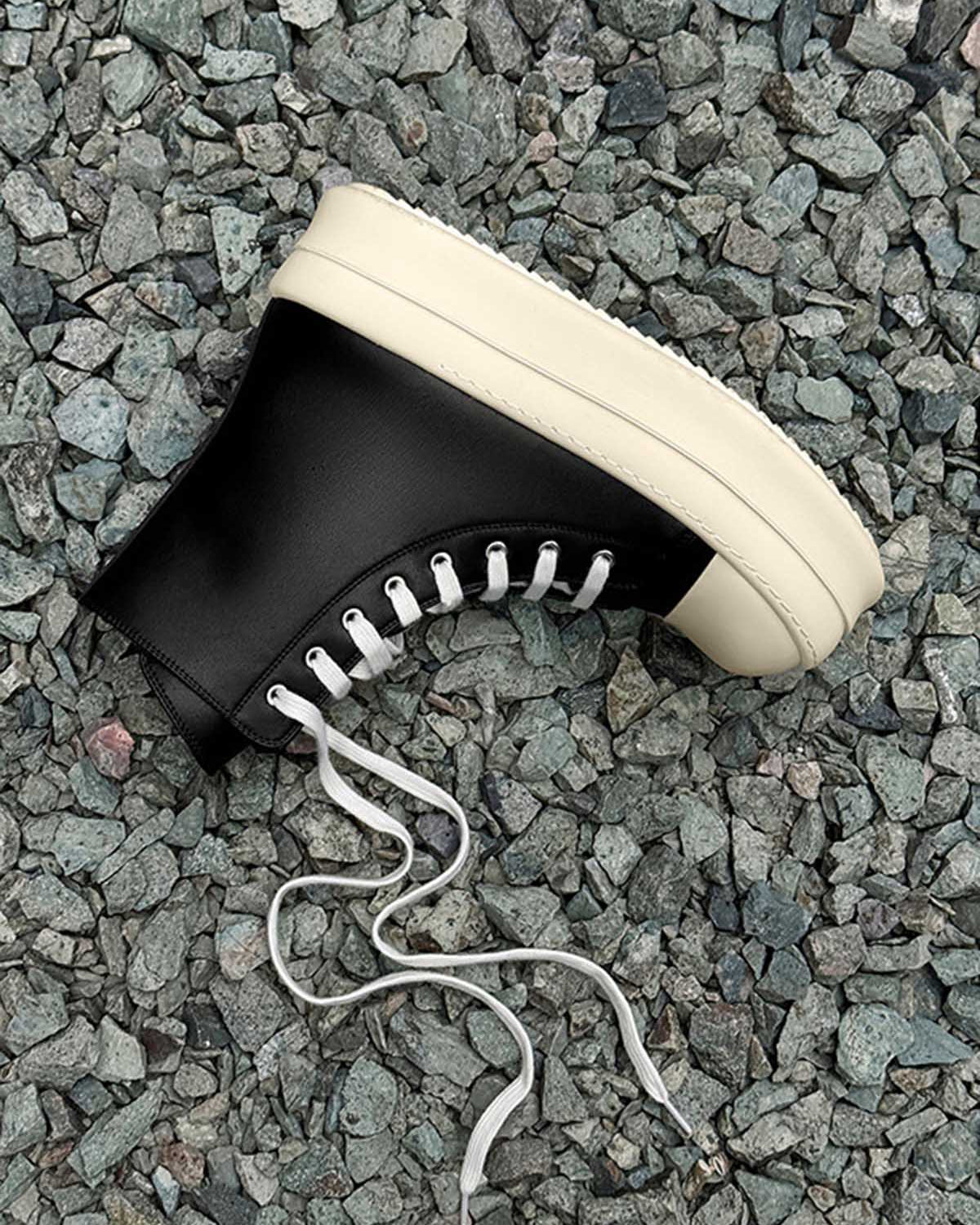 High-Top Platform Streetwear Sneakers on gray stones, featuring a black high-top design with an off-white platform sole and loosely trailing white laces.
