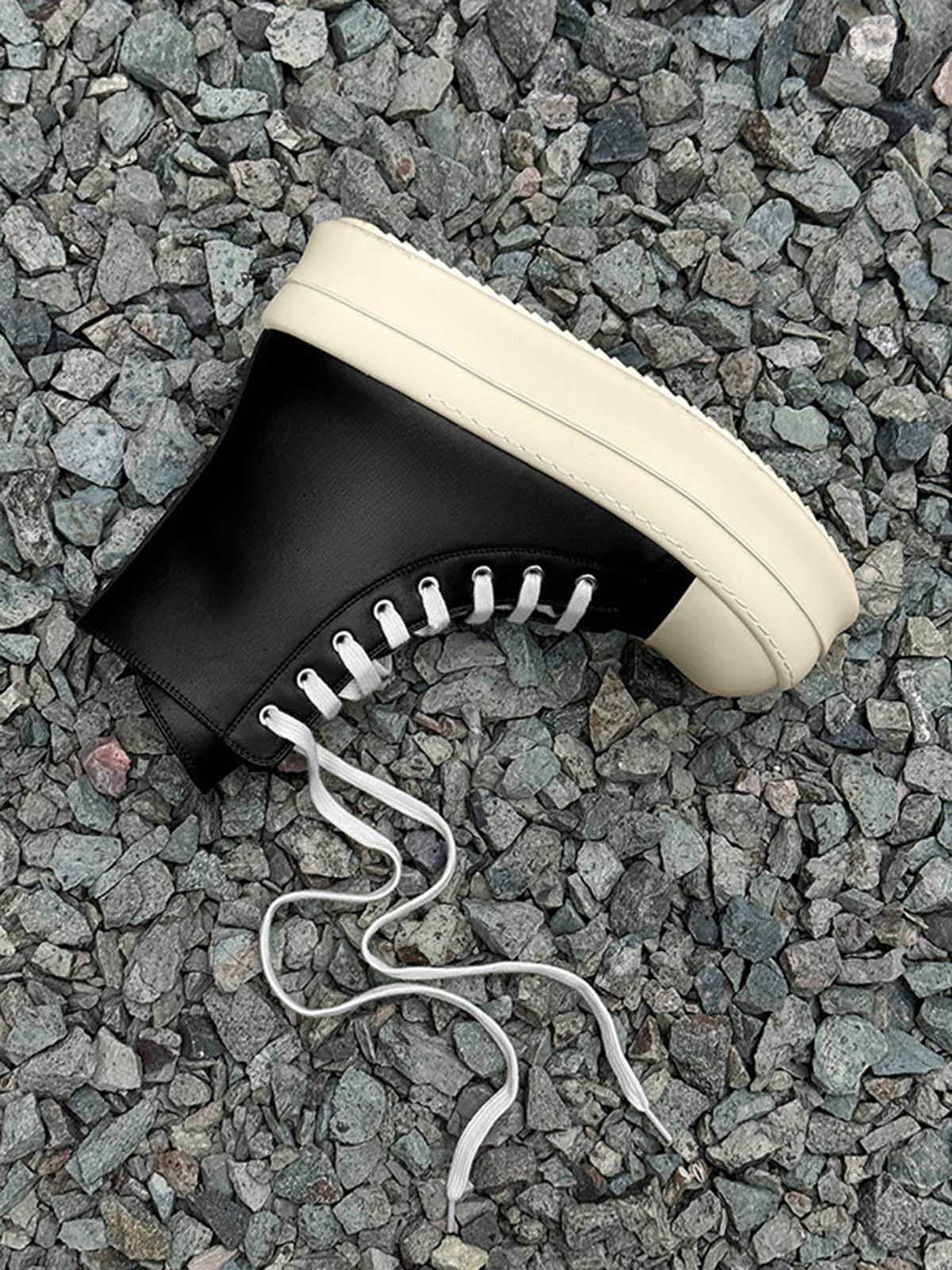 High-Top Platform Streetwear Sneakers on gray stones, featuring a black high-top design with an off-white platform sole and loosely trailing white laces.