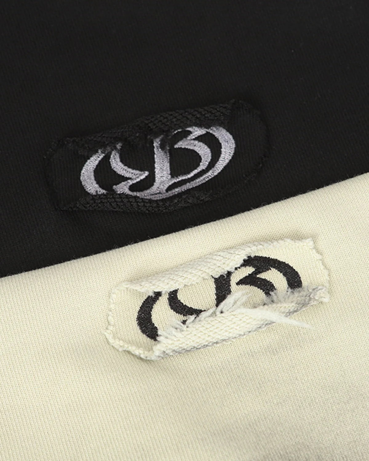 Close-up of Ink Dyed Raw-Edge Streetwear Hoodie tags, showcasing contrasting embroidered logos on black and off-white fabric, highlighting the brand's bold streetwear aesthetic.