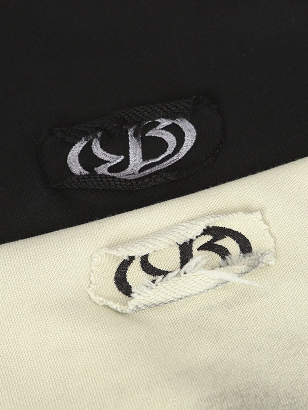 Close-up of Ink Dyed Raw-Edge Streetwear Hoodie tags, showcasing contrasting embroidered logos on black and off-white fabric, highlighting the brand's bold streetwear aesthetic.