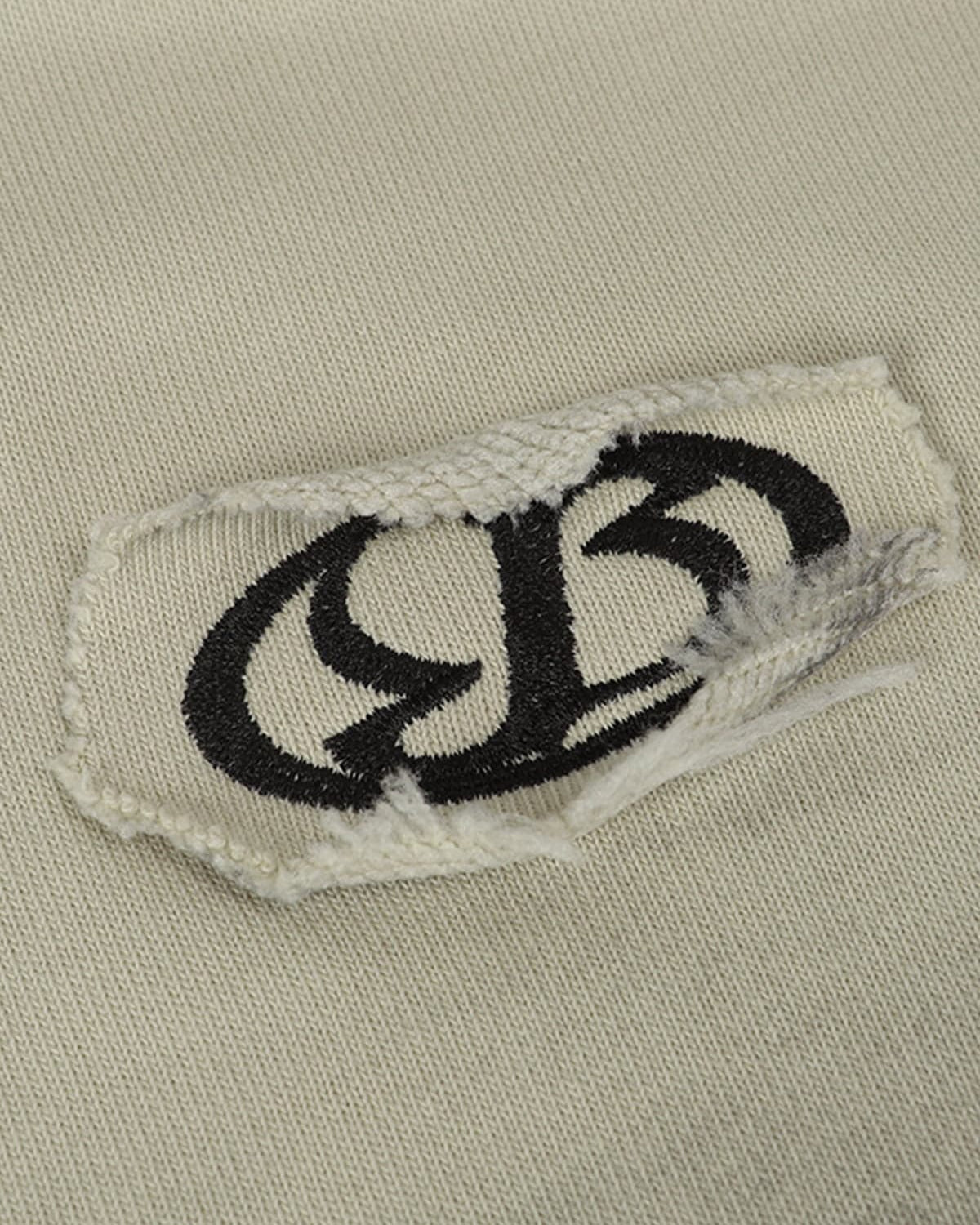 Close-up of Ink Dyed Raw-Edge Streetwear Hoodie featuring a beige knit fabric with a torn patch and frayed edges, showcasing a bold streetwear aesthetic.