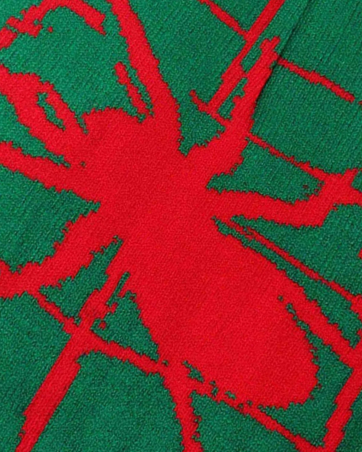 Close-up of the Spider Web Graphic Knit Hat featuring a green knit textile with a red, stylized spider silhouette, emphasizing its bold streetwear aesthetic.