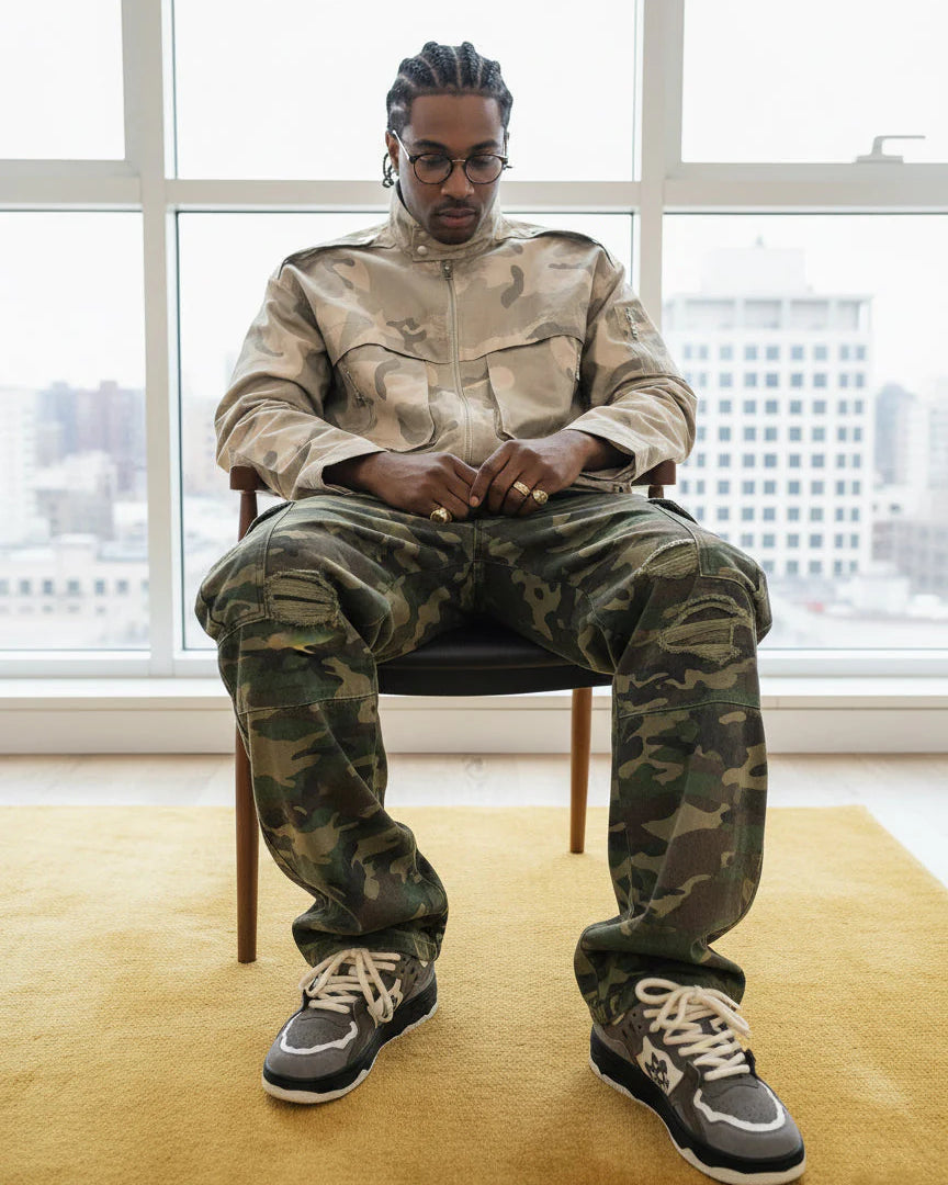 Person in camo attire wears Vintage Chunky Graphic Skate Shoes, featuring a bold, chunky silhouette and thick rope laces, seated on a mustard rug by a window.