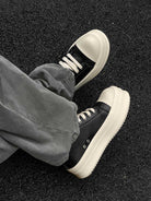 Chunky Low-Top Streetwear Sneakers featuring black uppers and cream chunky soles, worn with gray pants, embodying bold, modern streetwear style with German-trainer inspiration.