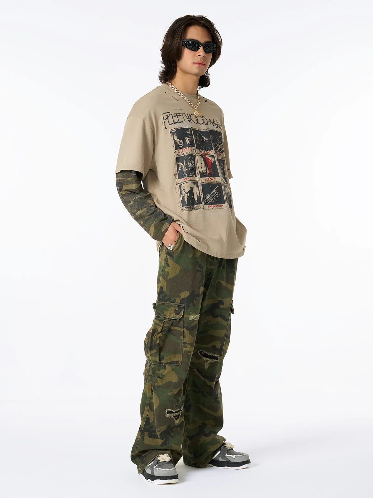 Model in Distressed Grunge Layered T-Shirt with graphic design, camo long sleeves, camouflage cargo pants, chunky sneakers, gold chain, sunglasses, and silver ring.