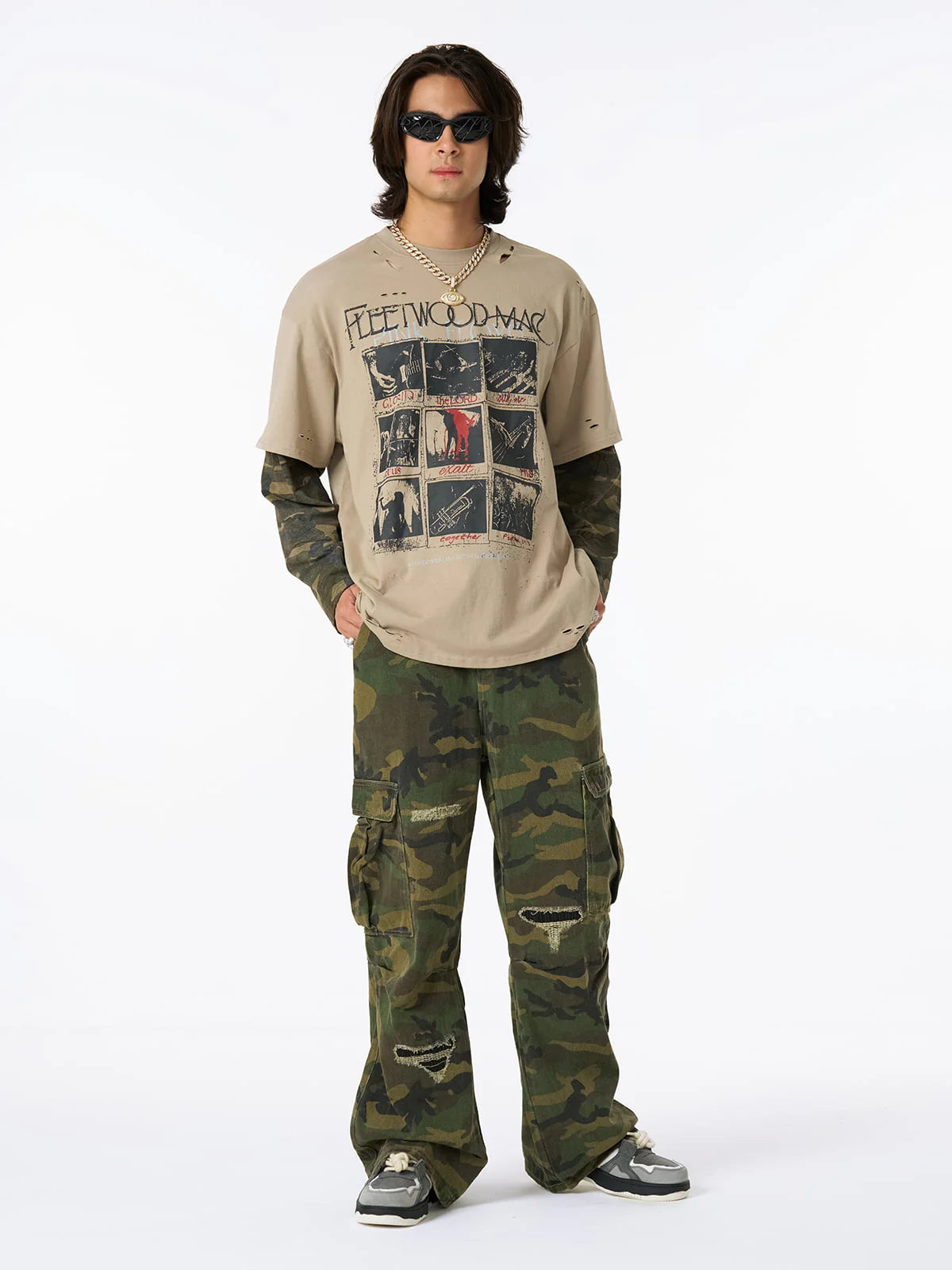 Young man models Distressed Grunge Layered T-Shirt with vintage Fleetwood Mac print, camo long sleeves, and intentional distressing, styled with camo pants and chunky sneakers.