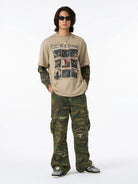 Young man models Distressed Grunge Layered T-Shirt with vintage Fleetwood Mac print, camo long sleeves, and intentional distressing, styled with camo pants and chunky sneakers.