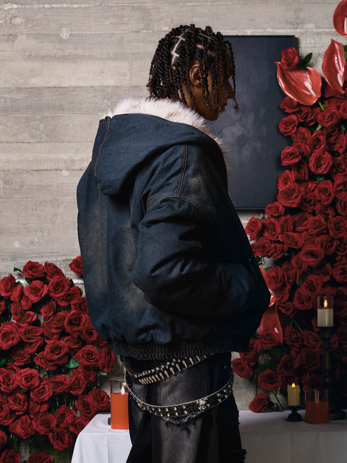Person in profile wearing the Distressed Washed Faux Fur Winter Jacket with a fluffy collar, styled with black pants and surrounded by roses and candles.