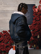 Person in profile wearing the Distressed Washed Faux Fur Winter Jacket with a fluffy collar, styled with black pants and surrounded by roses and candles.