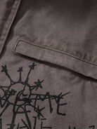 Graphic Graffiti High Neck Street Jacket highlighting a grey canvas-style fabric with a horizontal pocket flap and a black, hand-drawn sunburst graphic below it.