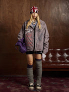 Young person indoors wearing Graphic Graffiti High Neck Street Jacket with graffiti-style lettering, layered look, shorts, over-the-knee legwarmers, and slouchy purple handbag.