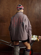Person wearing the Graphic Graffiti High Neck Street Jacket, showcasing bold graffiti designs and a high-neck silhouette, while pushing a wheelbarrow filled with roses indoors.