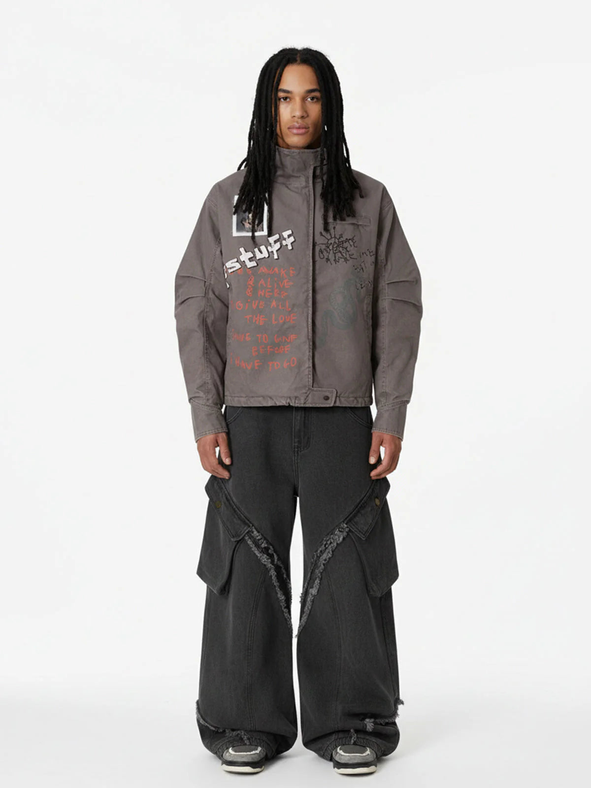 Young man wearing a Graphic Graffiti High Neck Street Jacket with hand-drawn graphics, wide-leg black cargo jeans, and chunky sneakers, showcasing bold streetwear style.