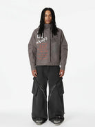 Young man wearing a Graphic Graffiti High Neck Street Jacket with hand-drawn graphics, wide-leg black cargo jeans, and chunky sneakers, showcasing bold streetwear style.