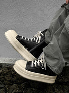 High-Top Platform Streetwear Sneakers with cream platform soles, white laces, and side zippers, worn with olive-green pants against a textured wall.