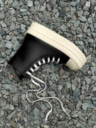 High-Top Platform Streetwear Sneakers on gray stones, featuring a black high-top design with an off-white platform sole and loosely trailing white laces.