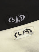 Close-up of Ink Dyed Raw-Edge Streetwear Hoodie tags, showcasing contrasting embroidered logos on black and off-white fabric, highlighting the brand's bold streetwear aesthetic.