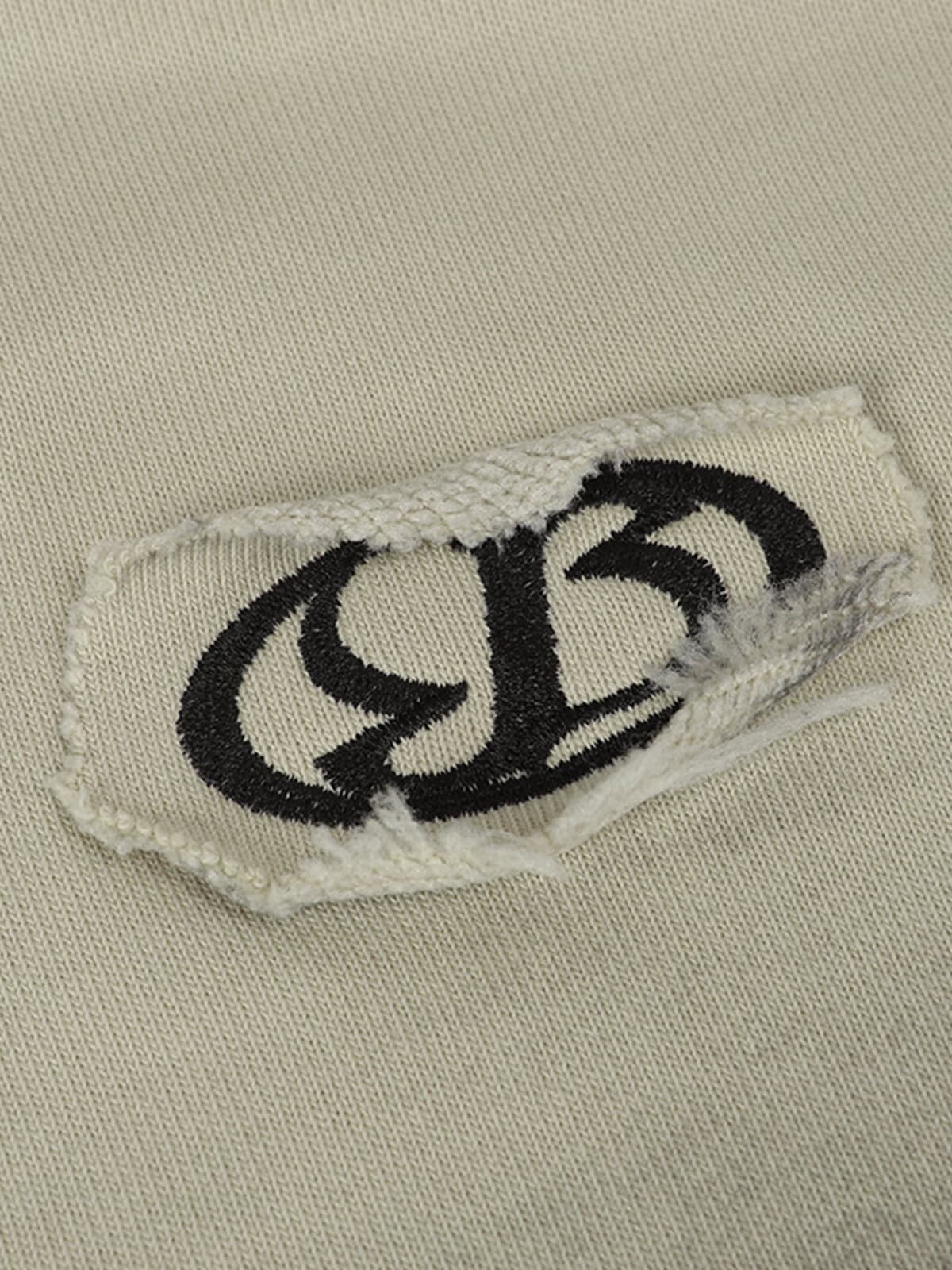 Close-up of Ink Dyed Raw-Edge Streetwear Hoodie featuring a beige knit fabric with a torn patch and frayed edges, showcasing a bold streetwear aesthetic.