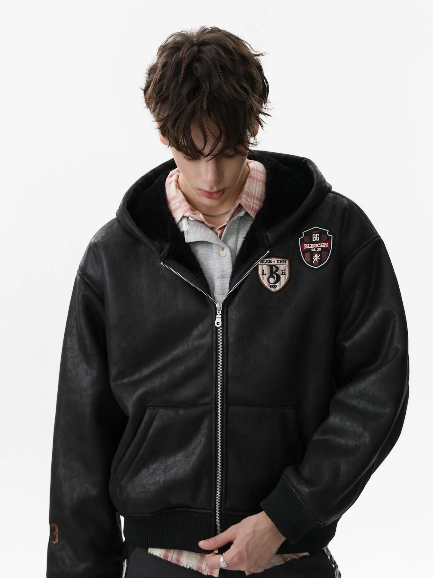 Young man in a Vintage Hooded Leather-Look Street Jacket with shearling-lined hood, vintage patches, layered over a plaid shirt, showcasing street style.