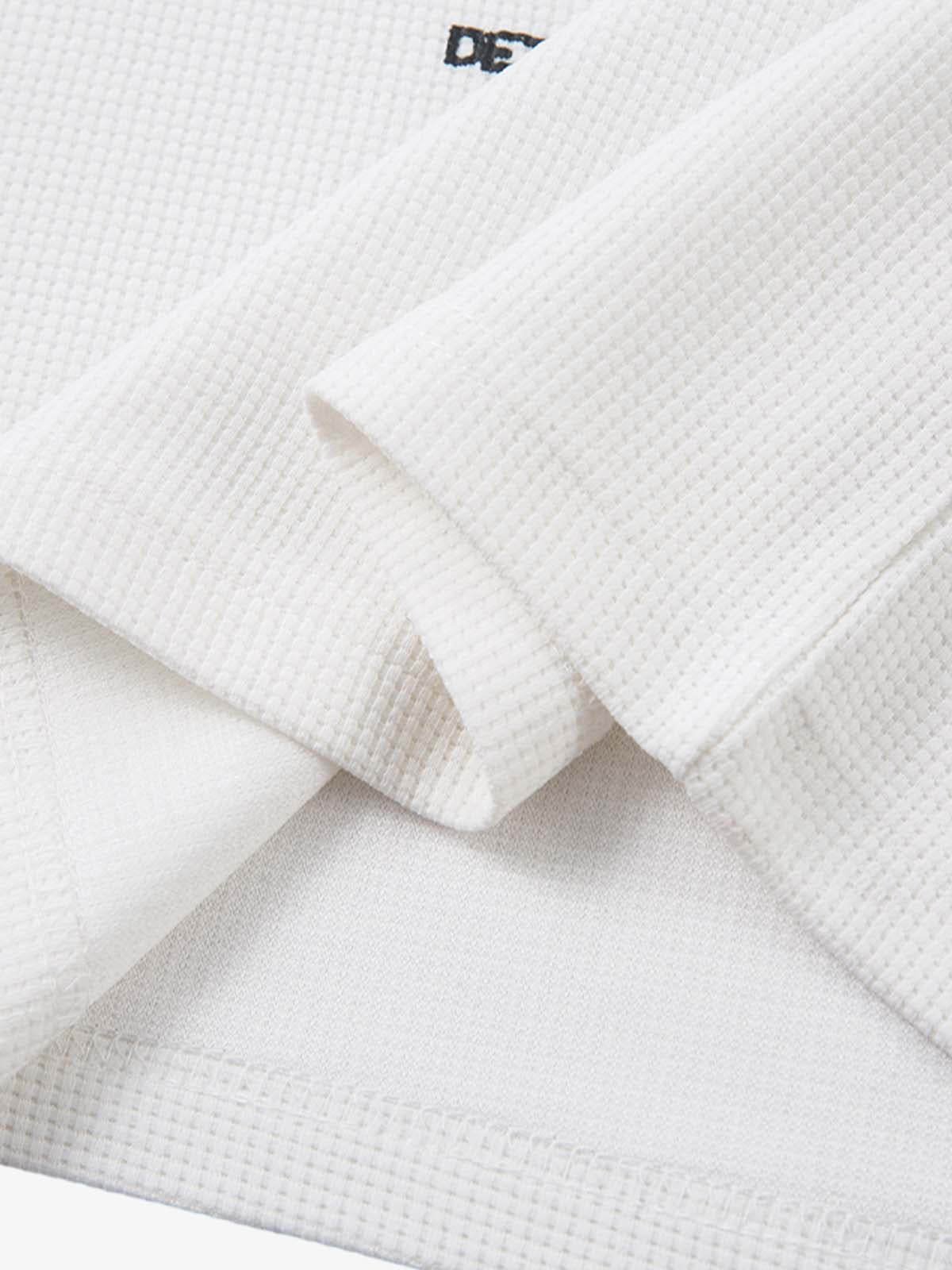 White Waffle Cross Graphic Long Sleeve T-Shirt showcasing waffle-knit texture, bold cross graphics, and a relaxed fit, embodying vintage streetwear and grunge styling.